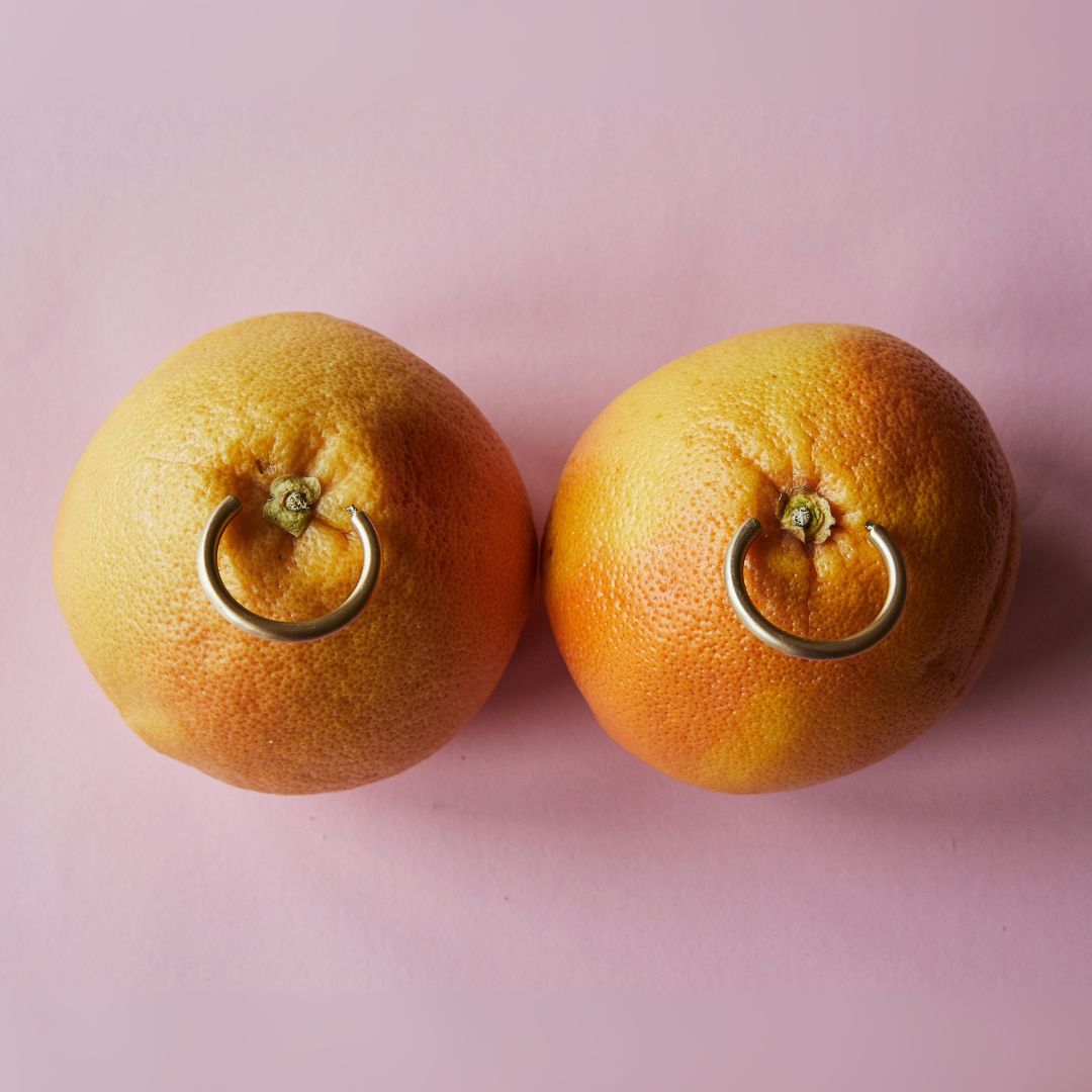Two oranges with gold rings on a pink background