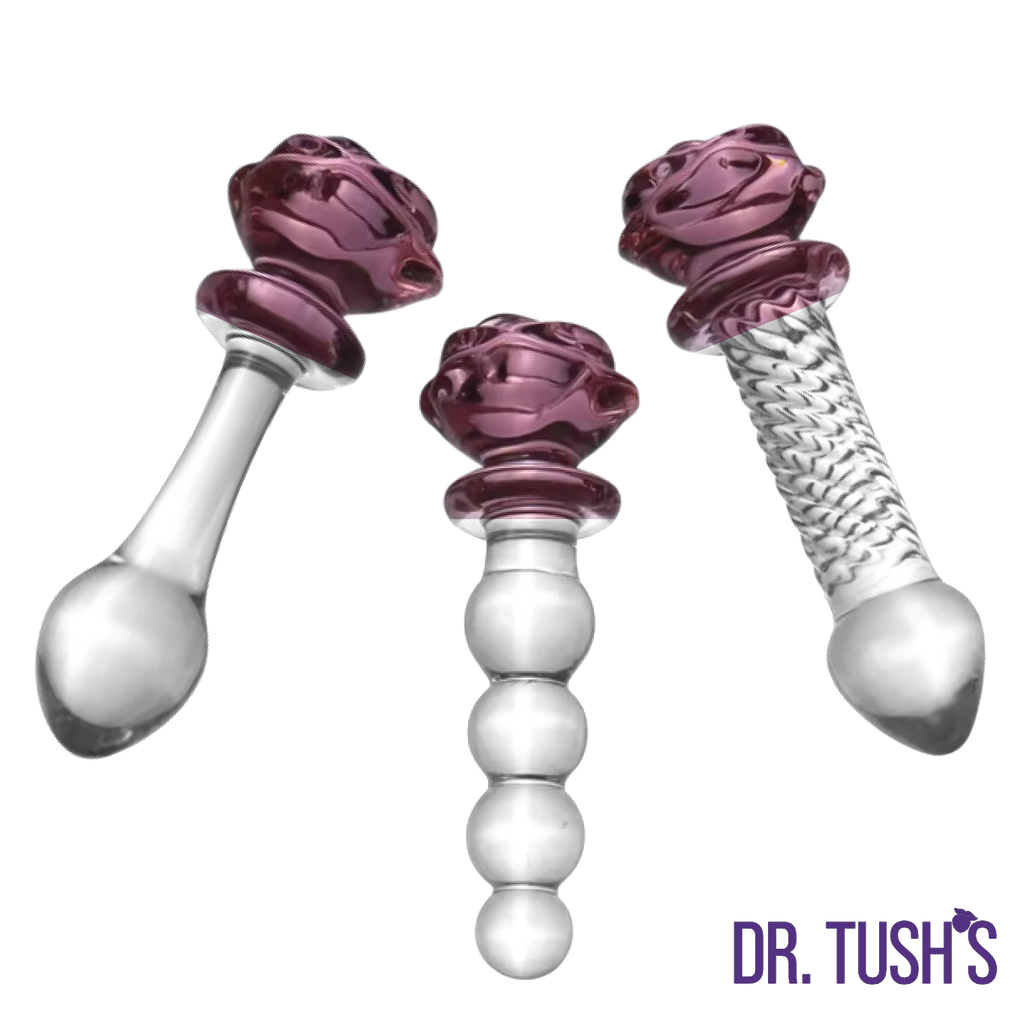 Three glass butt plugs and glass dildo with purple rose top and clear design on a white background, branded 'Dr. Tush'.