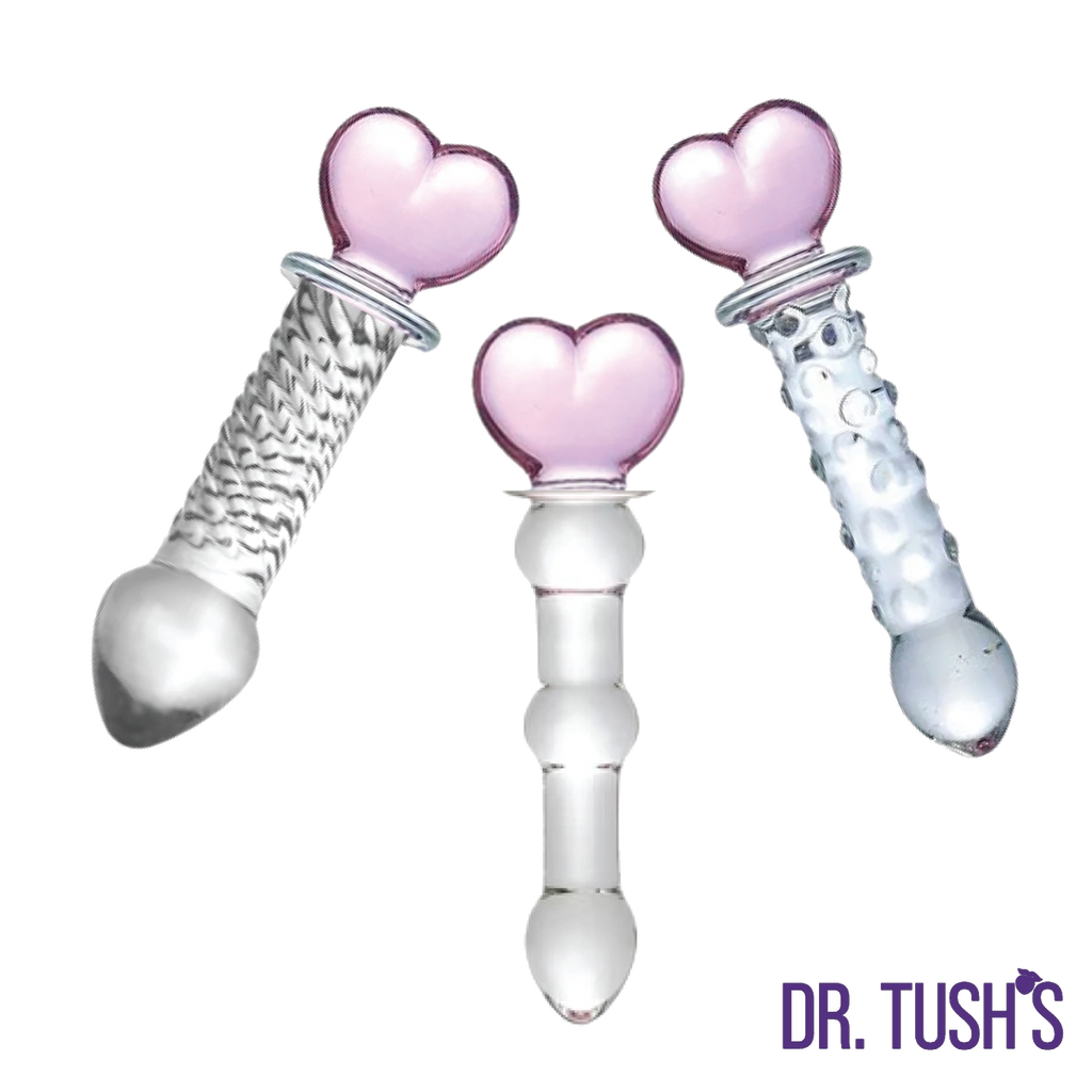 Three glass butt plugs with pink heart shaped top and glass dildo with and clear design on a white background, branded 'Dr. Tush'.