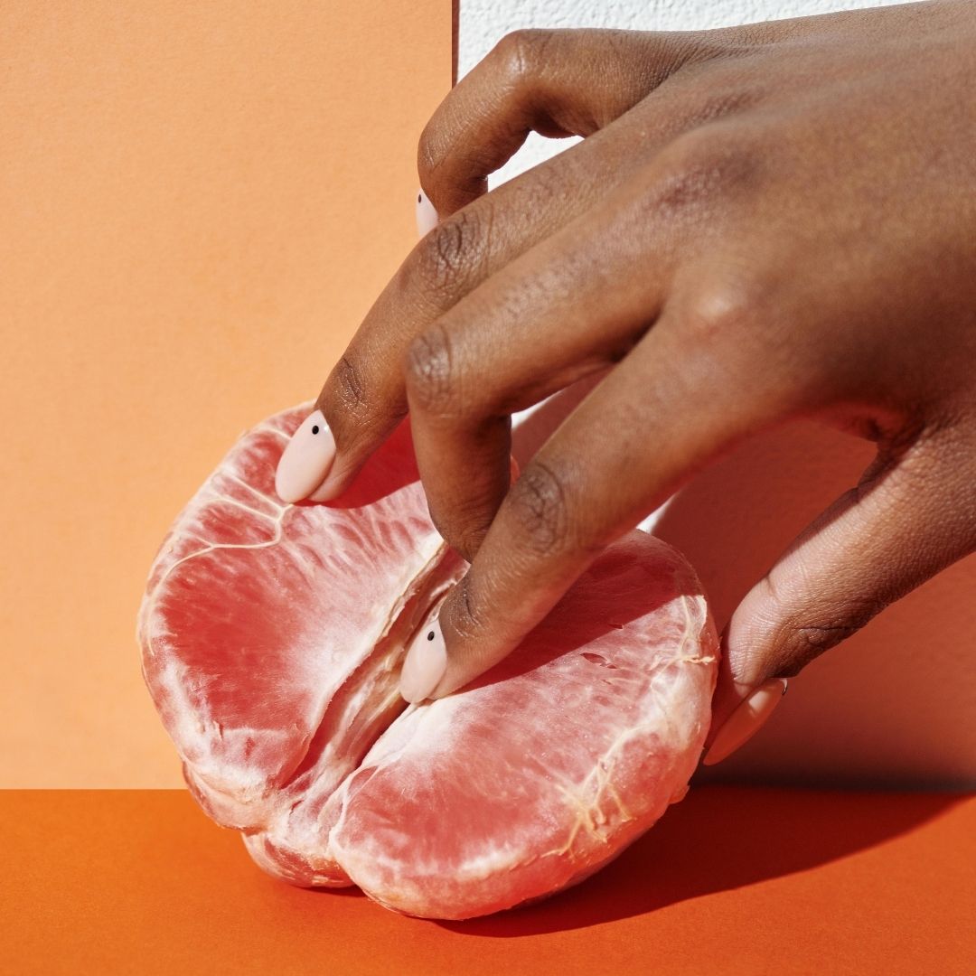 Hand holding a pink grapefruit against an orange background