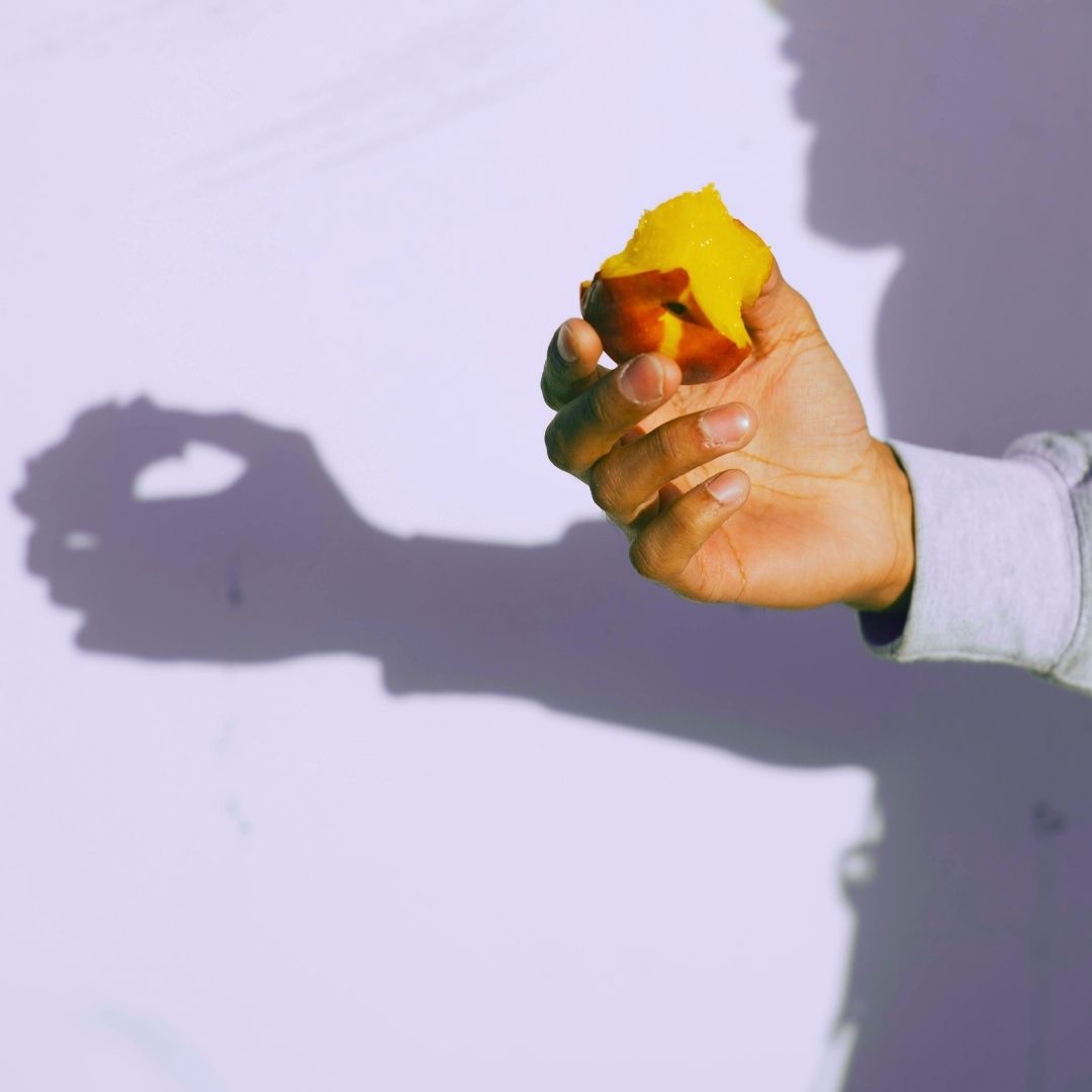 Hand holding a peach with bites taken out of it against a white background